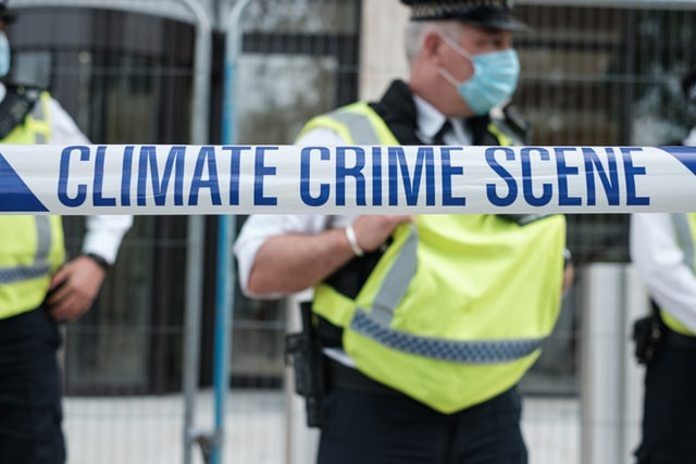 Policier derrière un ruban mentionnant "Climate crime scene"